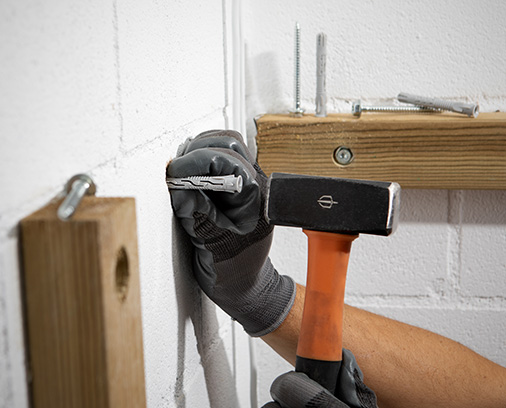 Bediener, der T-NUX-Dübel mit einem Hammer in die Wand einführt